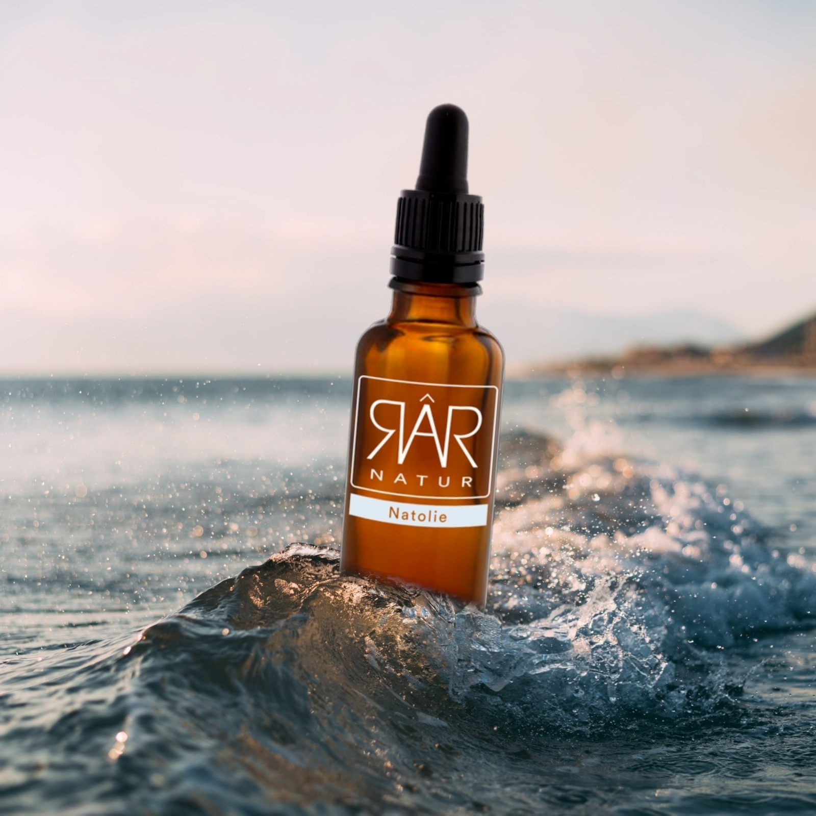 Pureday En brun dråbeflaske RAR Natolie - 30 ml sidder på toppen af en lille bølge i havet med en sløret kystbaggrund under solnedgang.