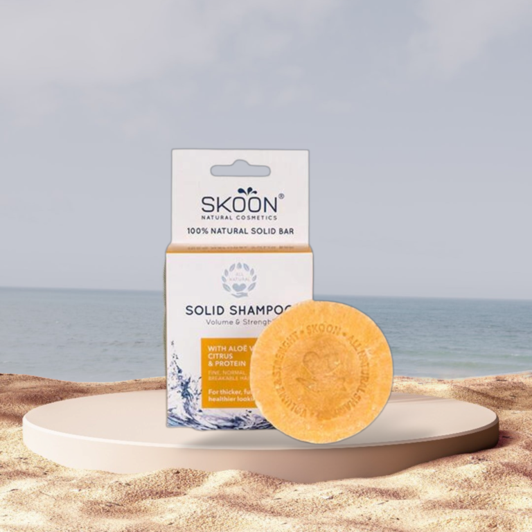Pureday En Skoon shampoobar - Volume & Strength VINDER I 2022 og dens emballage på et cirkulært stativ mod en strandbaggrund. Pakken kan prale af 100% naturlige ingredienser og er designet til volumen og sundere hår, hvilket fremmer optimal helbredelse.