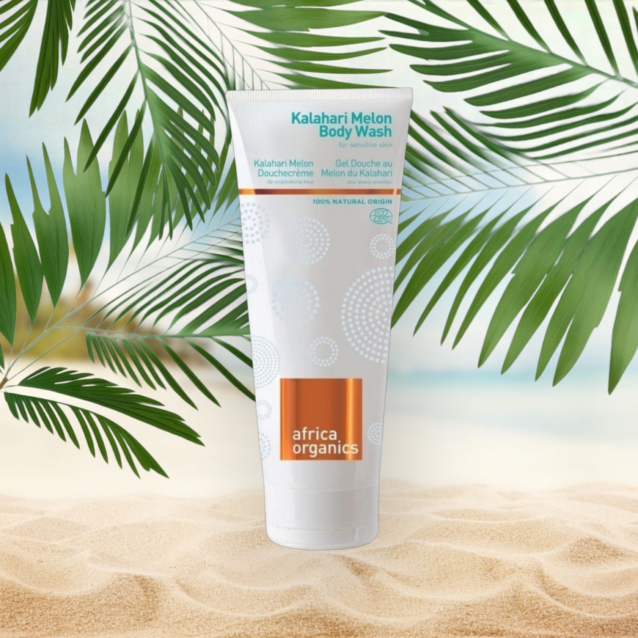 En tube Africa Organics Kalahari Melon Body Wash 210ml siddende på en strand med palmer.