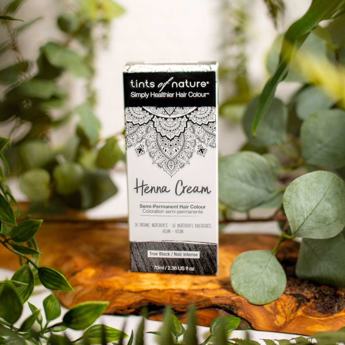 En æske Tints of Nature Henna Cream True Black - 70 ml siddende på et bord med planter, fremme sundhed og velvære.