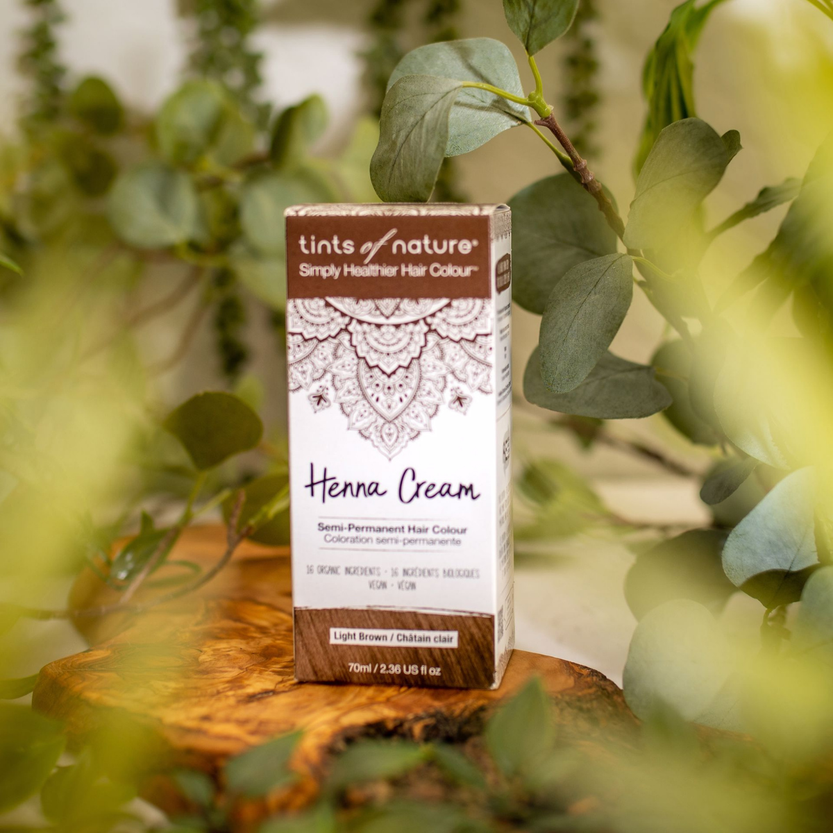 En æske Tints of Nature Henna Cream Light Brown - 70 ml siddende på et træbord.