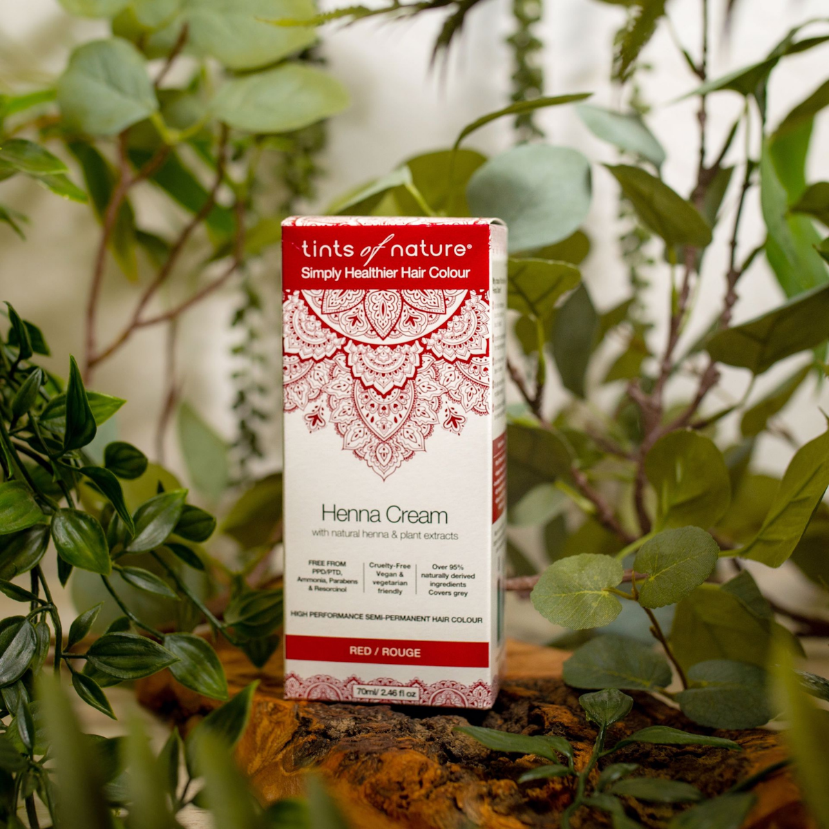 Pureday En æske Tints of Nature Henna Cream Red - 70 ml hårfarve, udstillet blandt frodige grønne planter på en træoverflade hos Matas.