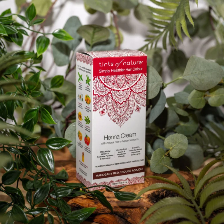 Pureday Æske med Tints of Nature Henna Cream Mahogany Red - 70 ml udstillet blandt grønne planter, med detaljerede røde og hvide paisley-designs på emballagen. Dette pureday-produkt tilbyder en naturlig.