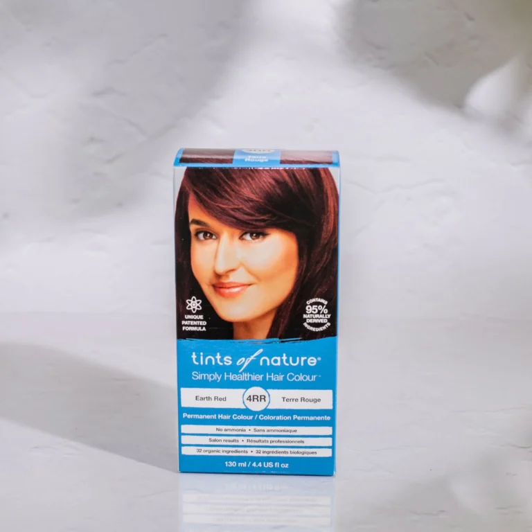 Pureday En æske med Tints of Nature 4RR Earth Red hårfarve på en marmoroverflade, med et billede af en kvinde med brunt hår. Boksteksten fremhæver 85 % naturlige ingredienser og permanent hårfarve.