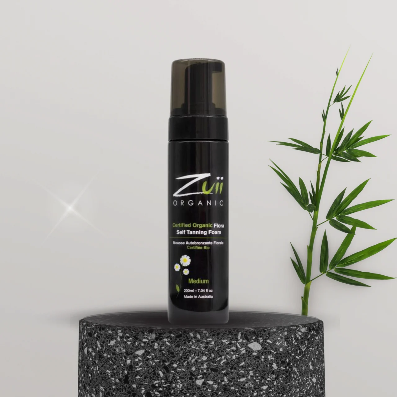 En flaske Zuii økologisk selvbruner mousse medium tilbud ved siden af en bambusplante, der giver en naturlig plejeoplevelse.