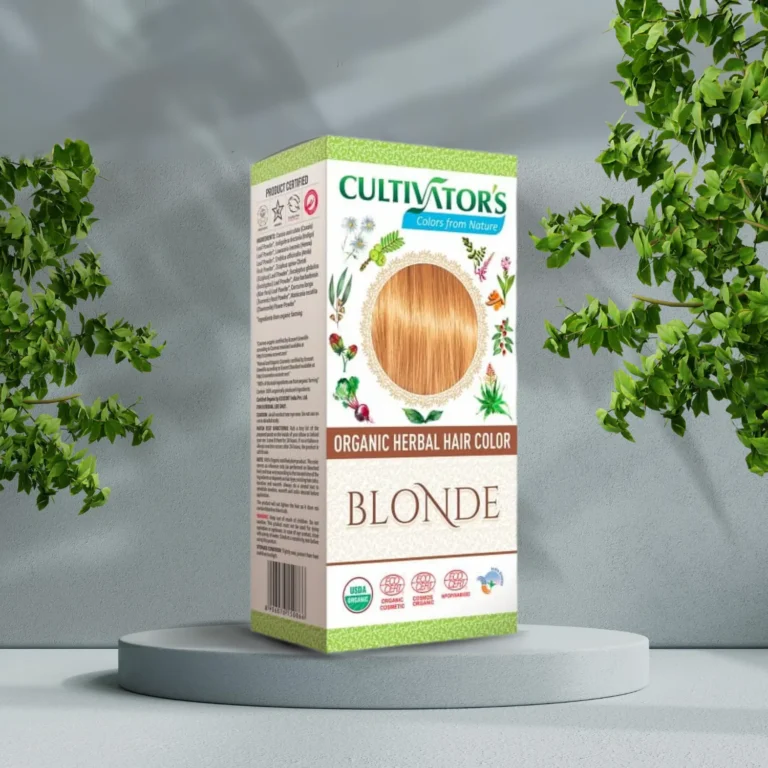 Pureday En æske med Cultivators Henna hårfarve Blonde 100g udstillet på en piedestal, med grønne buskede planter i baggrunden. Emballagen har naturlige farvelogoer, produktdetaljer.