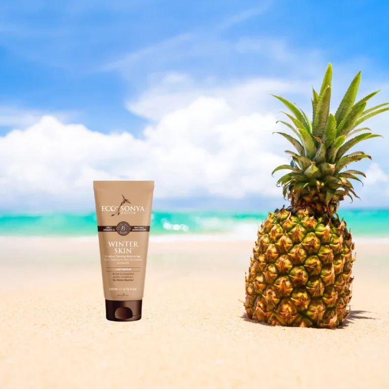 Pureday En flaske Winterskin - gradvis selvbruner lotion stående ved siden af en ananas på en sandstrand, med en klar blå himmel og turkisblåt hav i baggrunden.