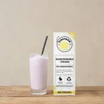 Pureday Et glas pink smoothie ved siden af en æske med 3 pakker Bionedbrydelige sugerør - plantebaseret 100 stk mærket "pureday" på et træbord mod en beige baggrund.