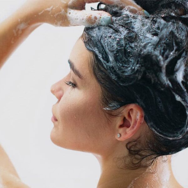 En kvinde vasker sit hår med Africa Organics - Mongongo Shampoo og balsam for en sund og luksuriøs selvplejerutine.